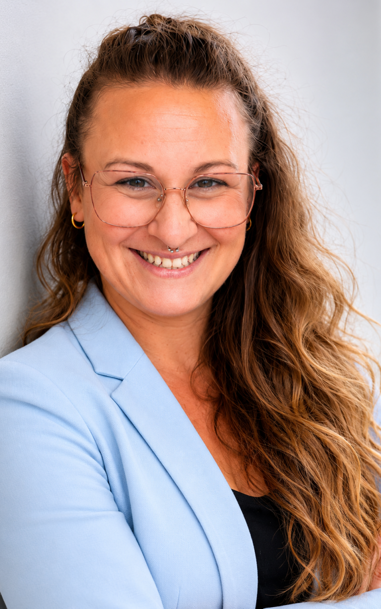 Lächelnde Person mit Brille und großen Ohrringen, hellem Oberteil und langen Haaren. Jeannine Schäfer
