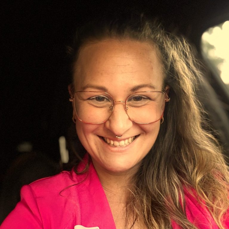 Lächelnde Person mit Brille und großen Ohrringen, hellem Oberteil und langen Haaren. Jeannine Schäfer